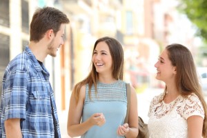 Three happy friends talking taking a conversation on the street in a sunny day with buildings in the background